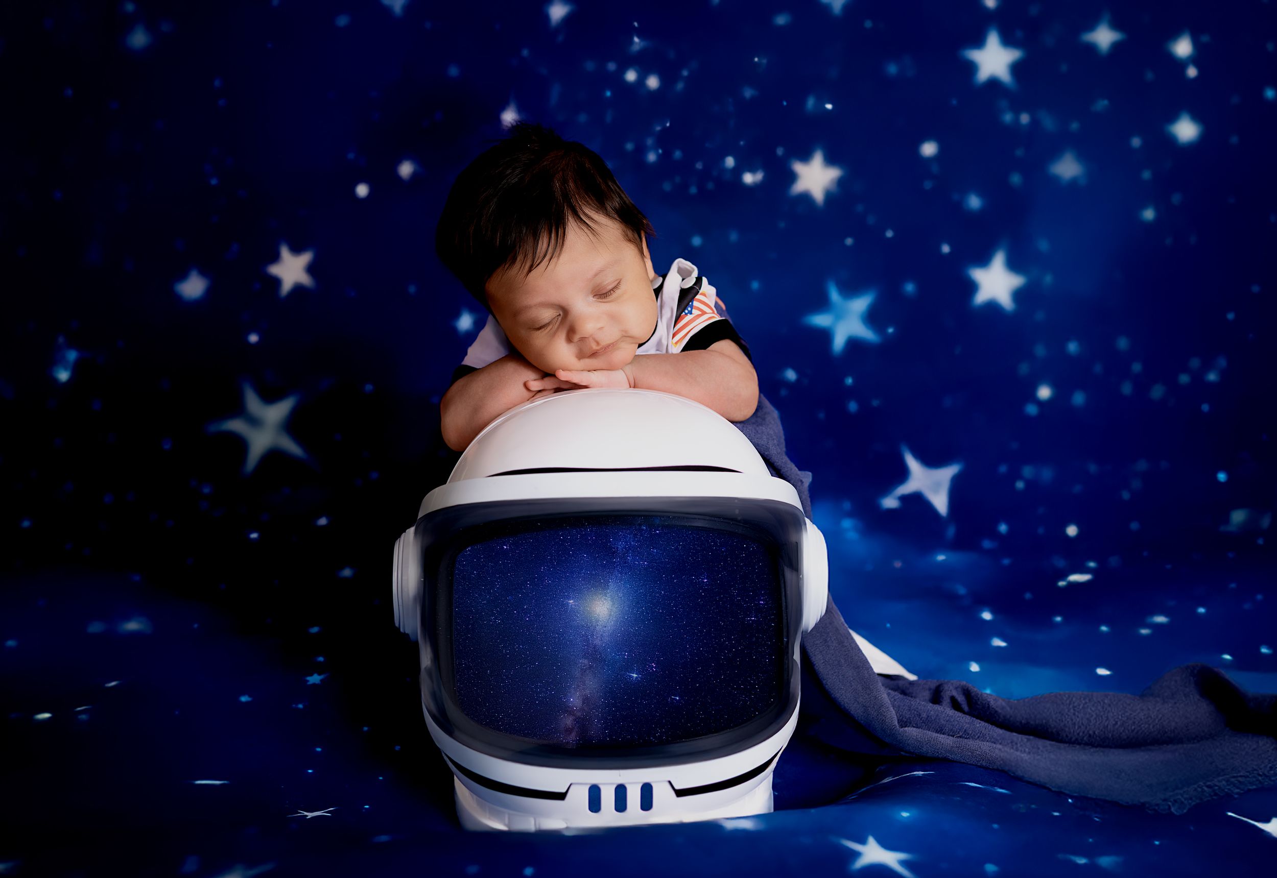 A series of seven photos showing a baby sleeping in a blue astronaut helmet against a starry background.