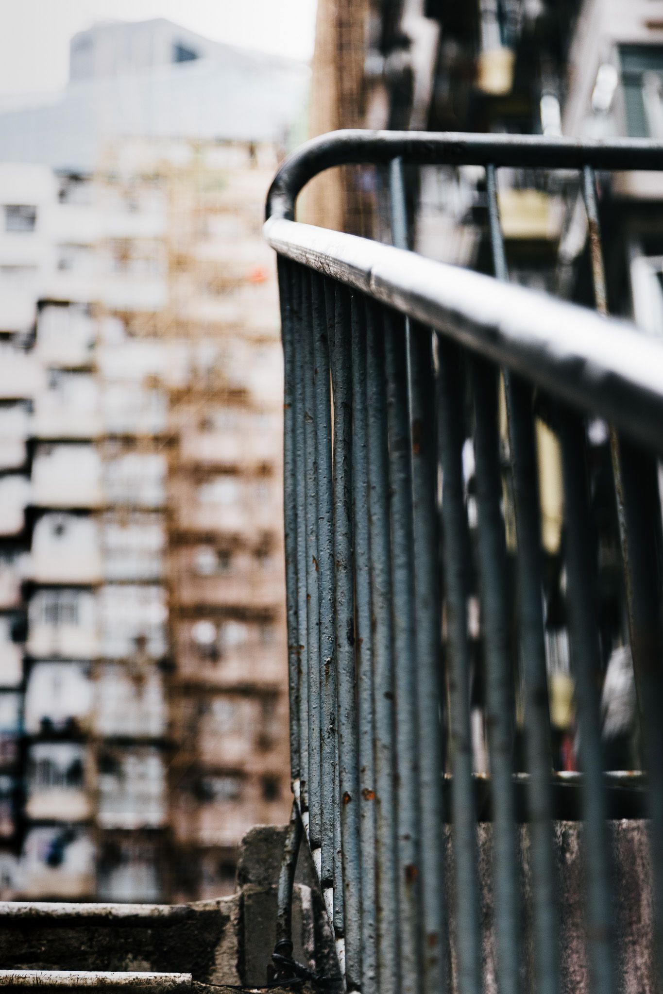 Close-up of weathered metal railings on urban stairs with blurred apartment buildings in background.