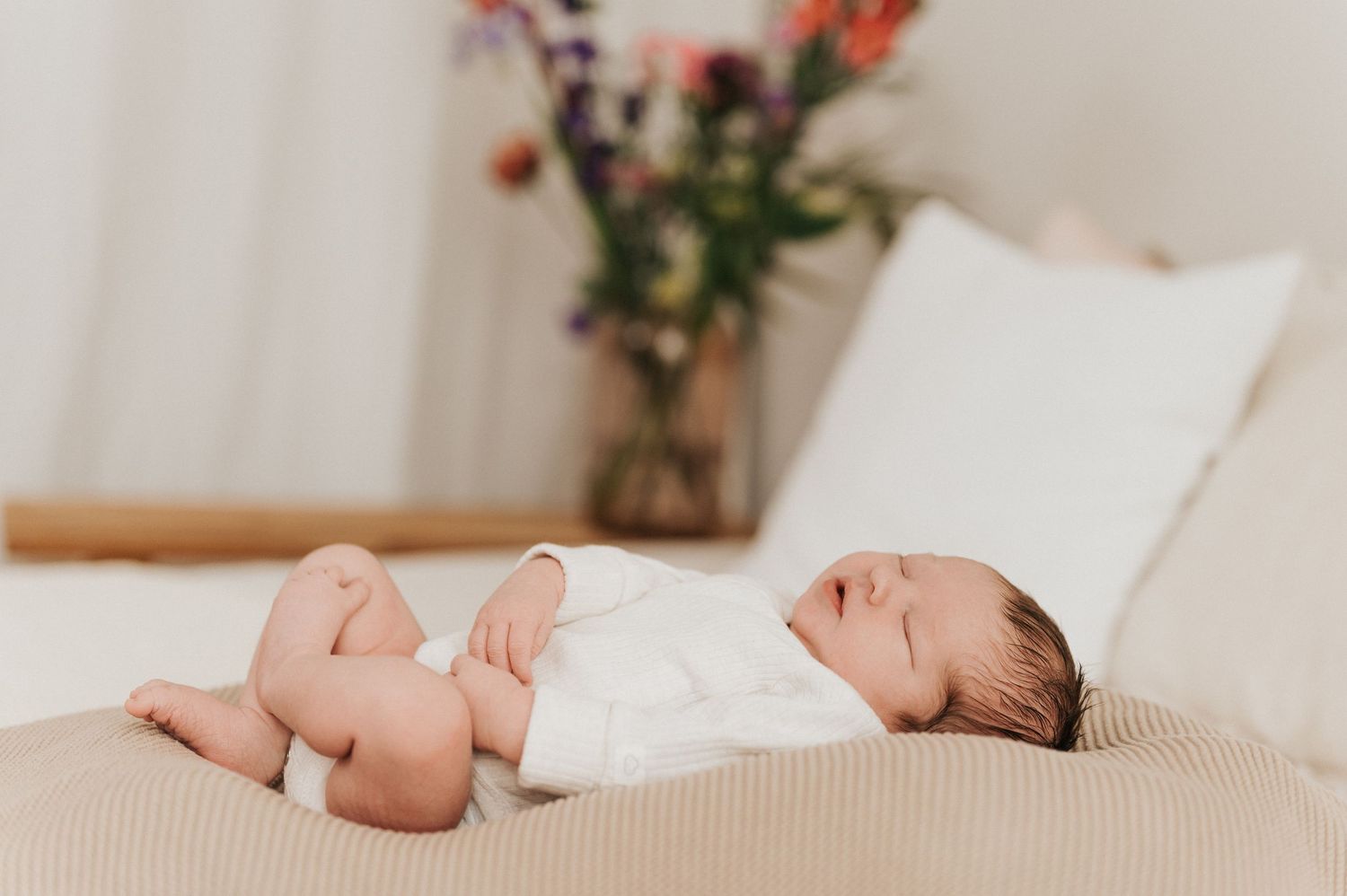 A sleeping newborn baby wrapped in soft white fabric with gentle hands providing comfort and support.