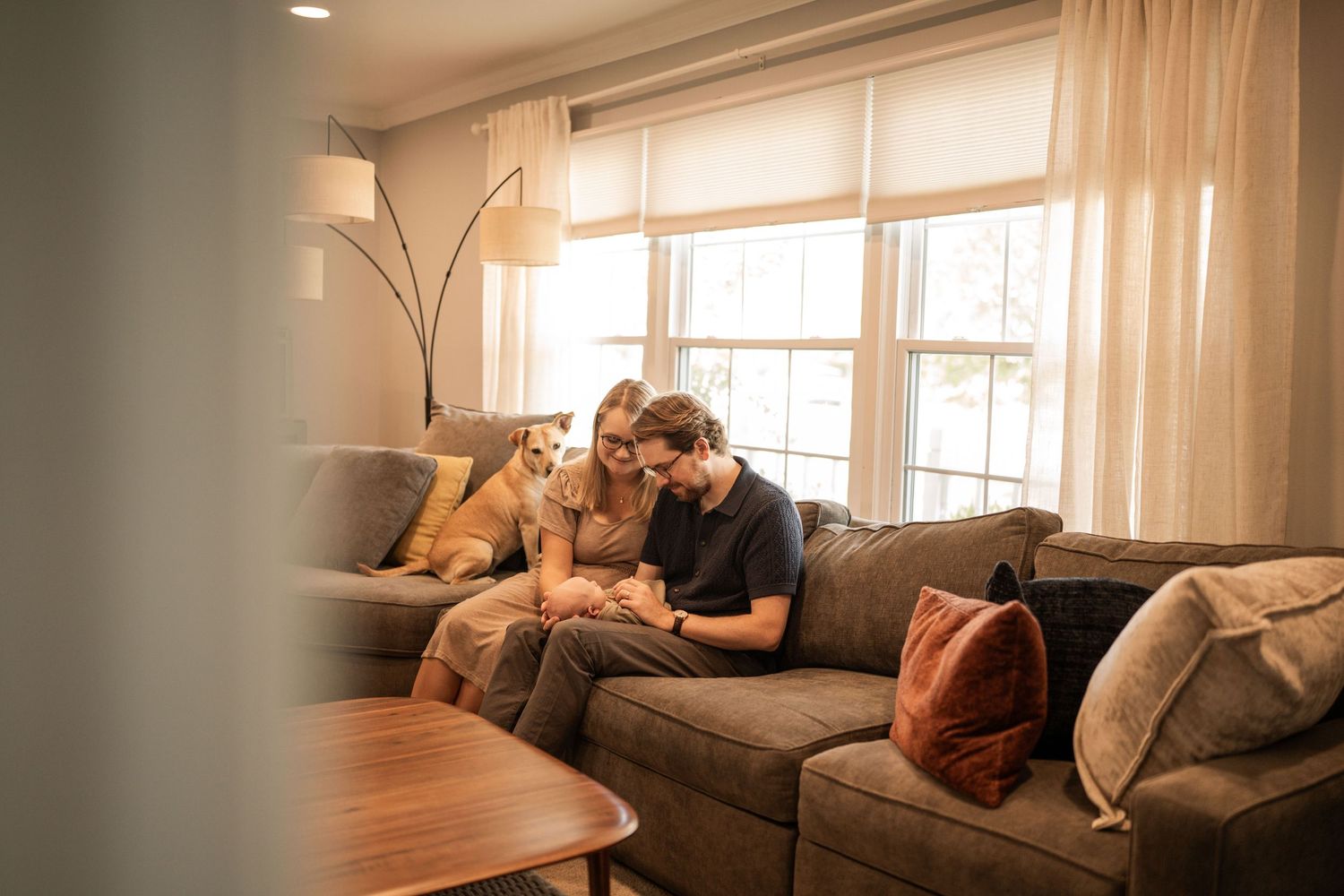 A cozy living room interior with warm lighting features new parents at a lifestyle photo session in Barrington