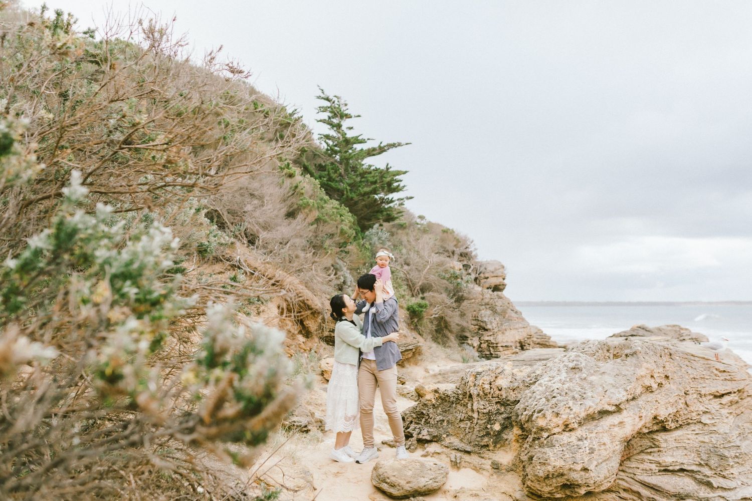Panoramic coastal path with white wooden railings overlooking misty rolling hills and ocean views.