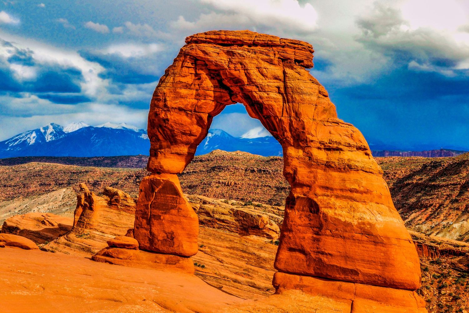 Natural sandstone arches glowing red against bright blue sky in desert landscape.