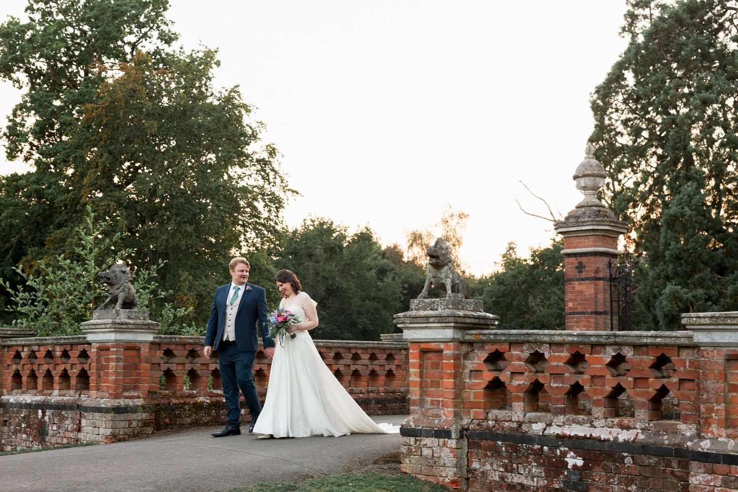 Wedding couple poses for photos along a decorative brick wall terrace at sunset.