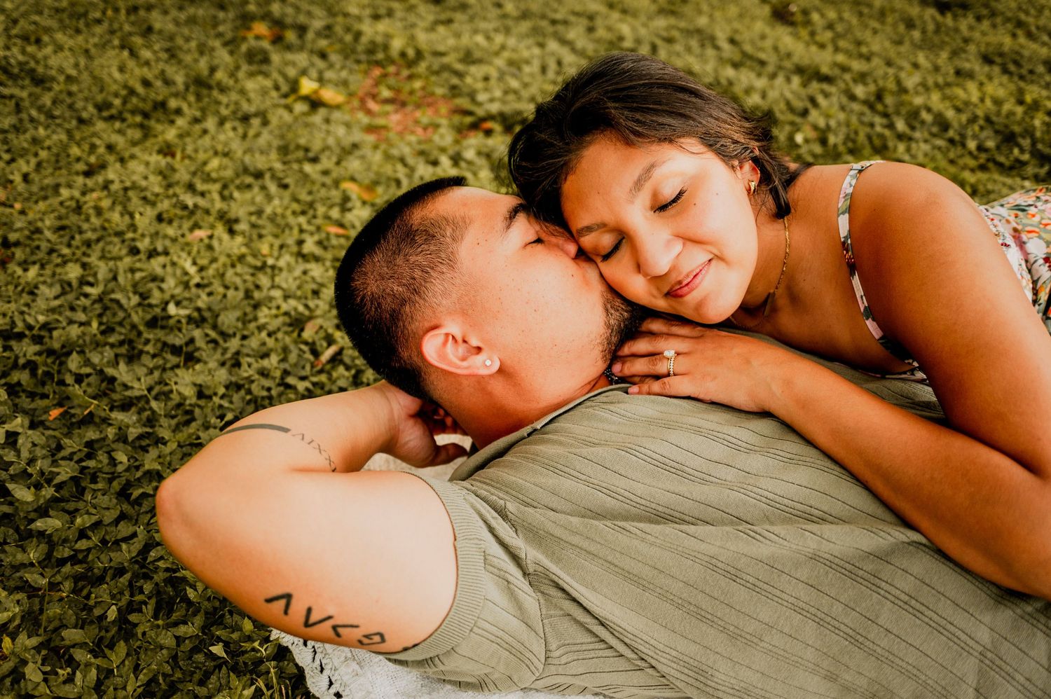 A couple lying on grass sharing an intimate moment in warm sunlight.