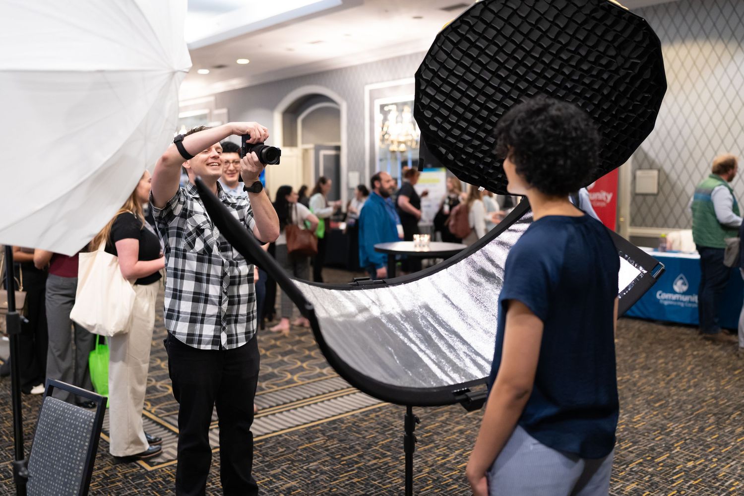 A photographer takes photos at an indoor event while attendees review materials in a hotel conference space.