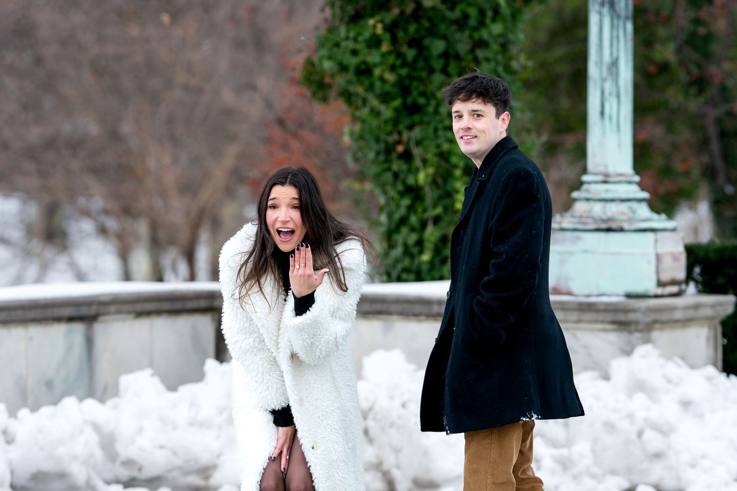 Surprised young woman in white coat and man in black coat posing in snowy park.