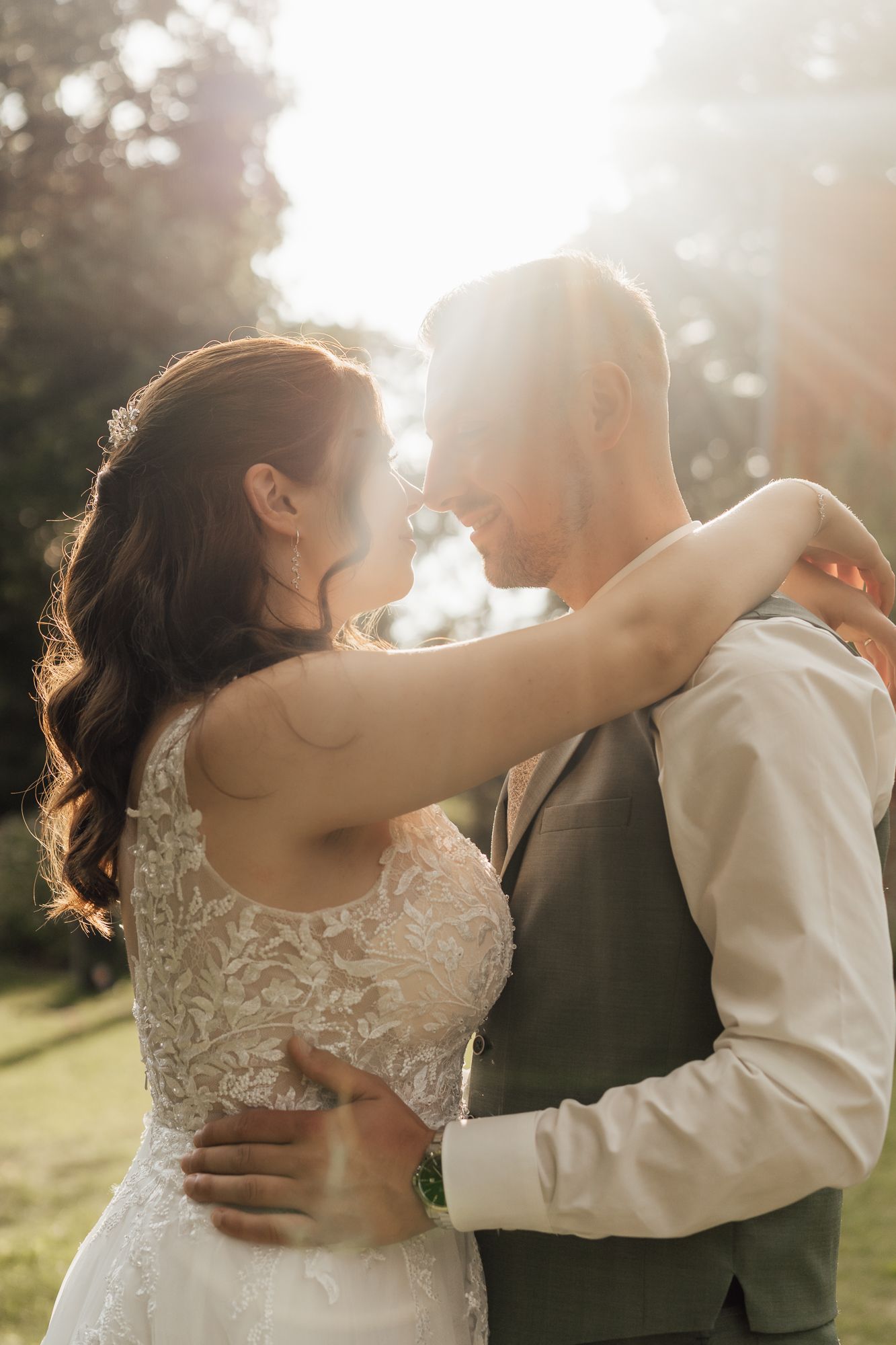 A romantic wedding couple embraces in sunlit garden setting at golden hour.