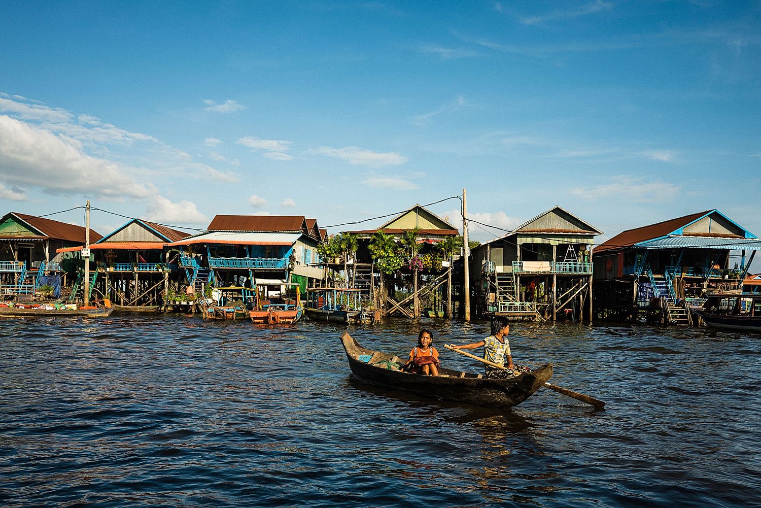 Traditional stilt houses line the waterfront as a small boat passes by on a sunny day.
