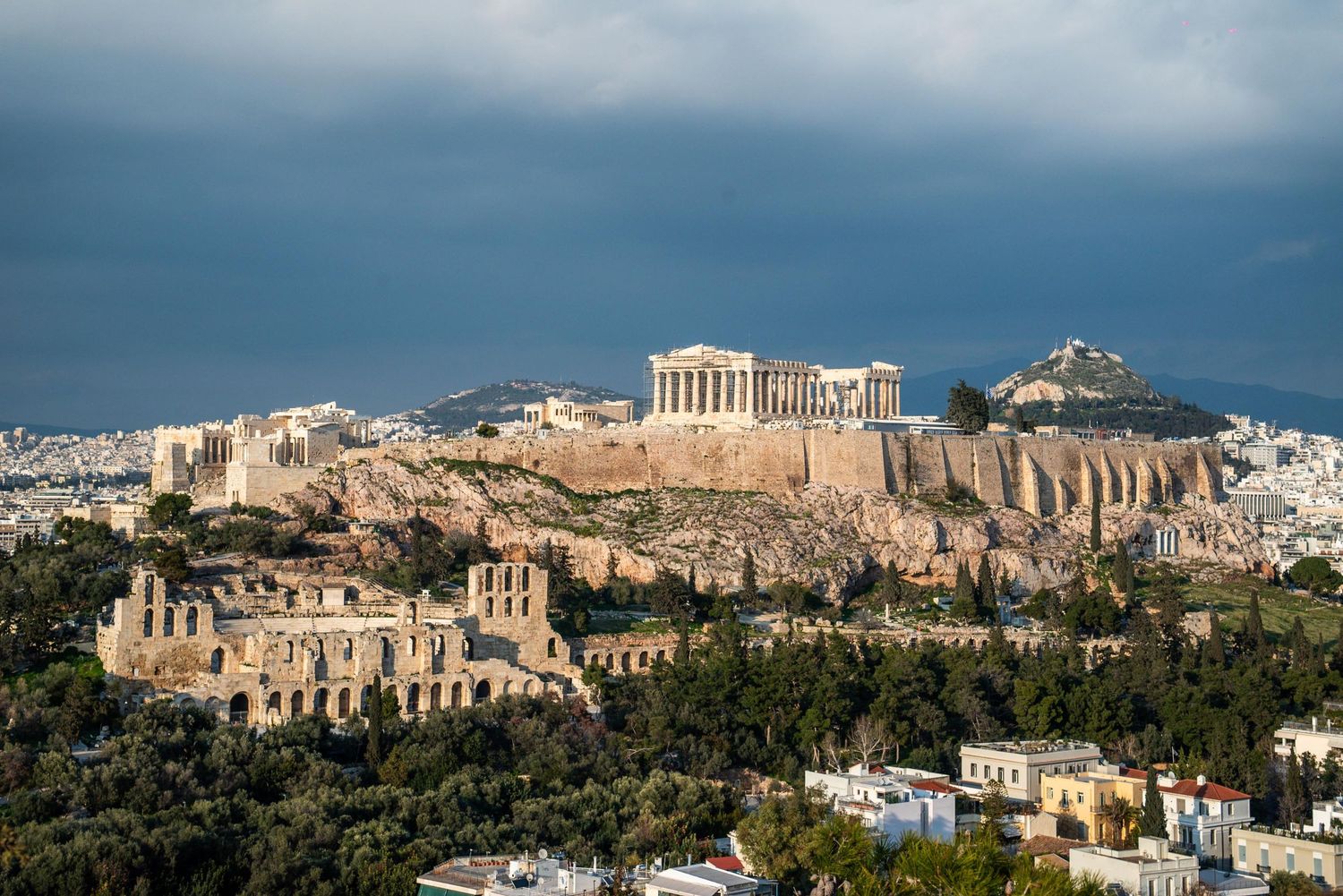 Ancient Acropolis and Parthenon temple stand majestically atop a rocky hill overlooking Athens at sunset.