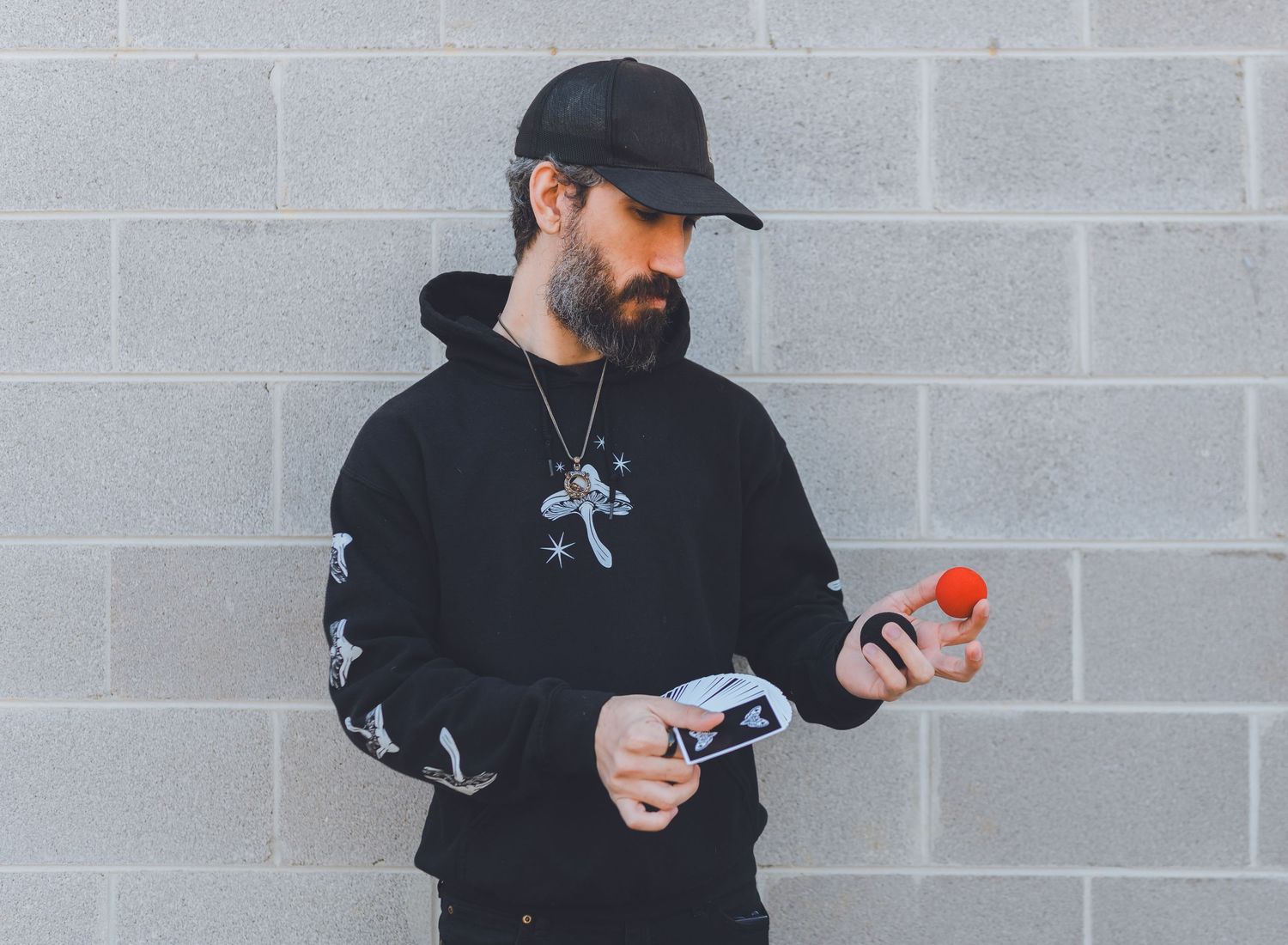 Person in black clothing and cap demonstrates a sequence of steps while holding gray and orange objects against a brick wall.