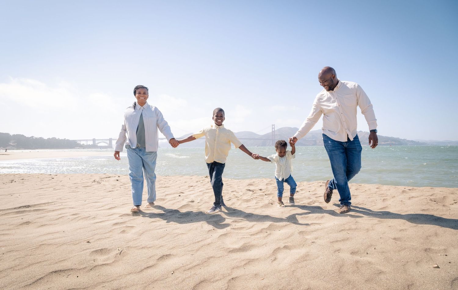 A family holding hands while walking together on a sunny beach along the ocean shoreline.