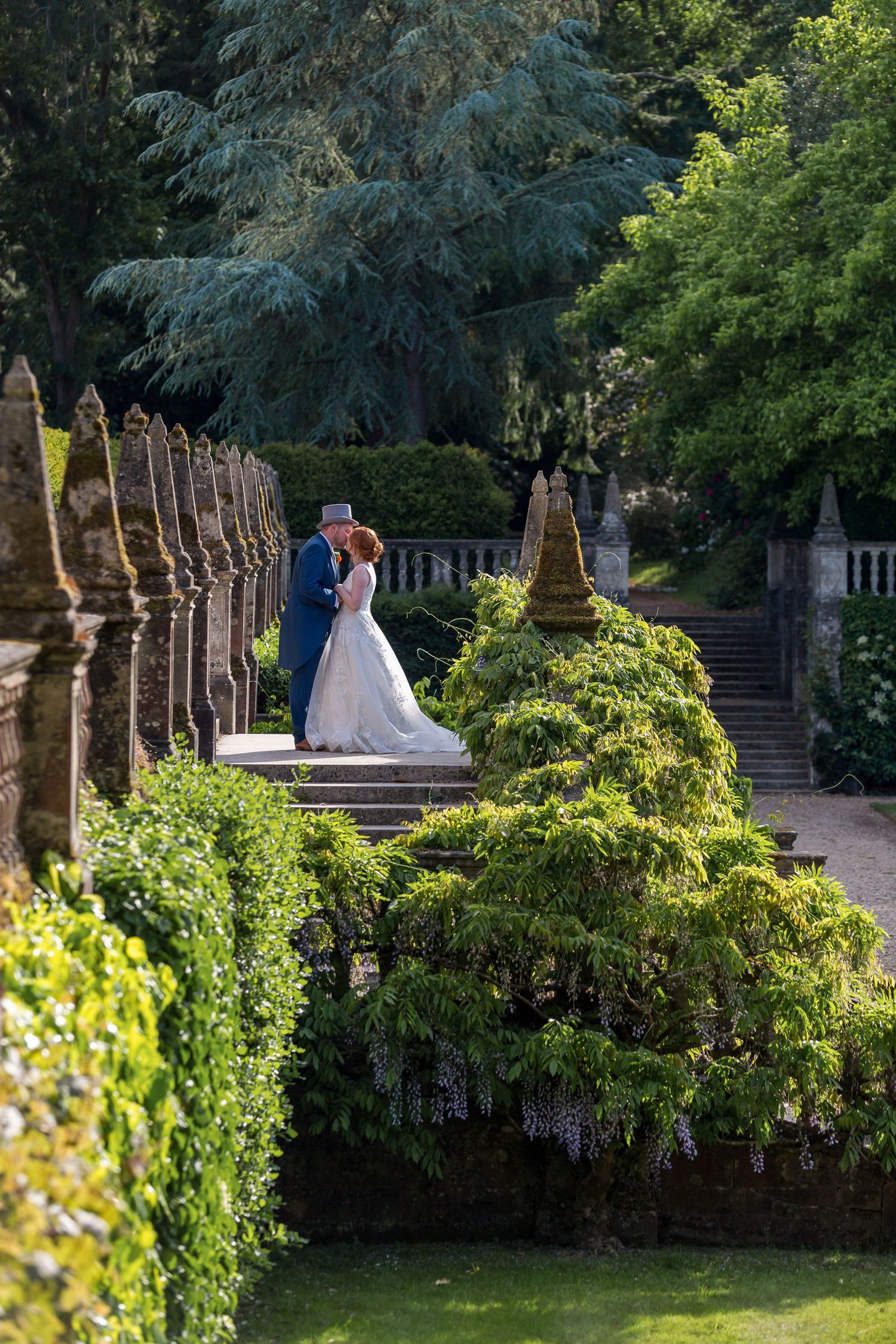 A couple walks through a scenic park with trees and a winding stream on their wedding day.