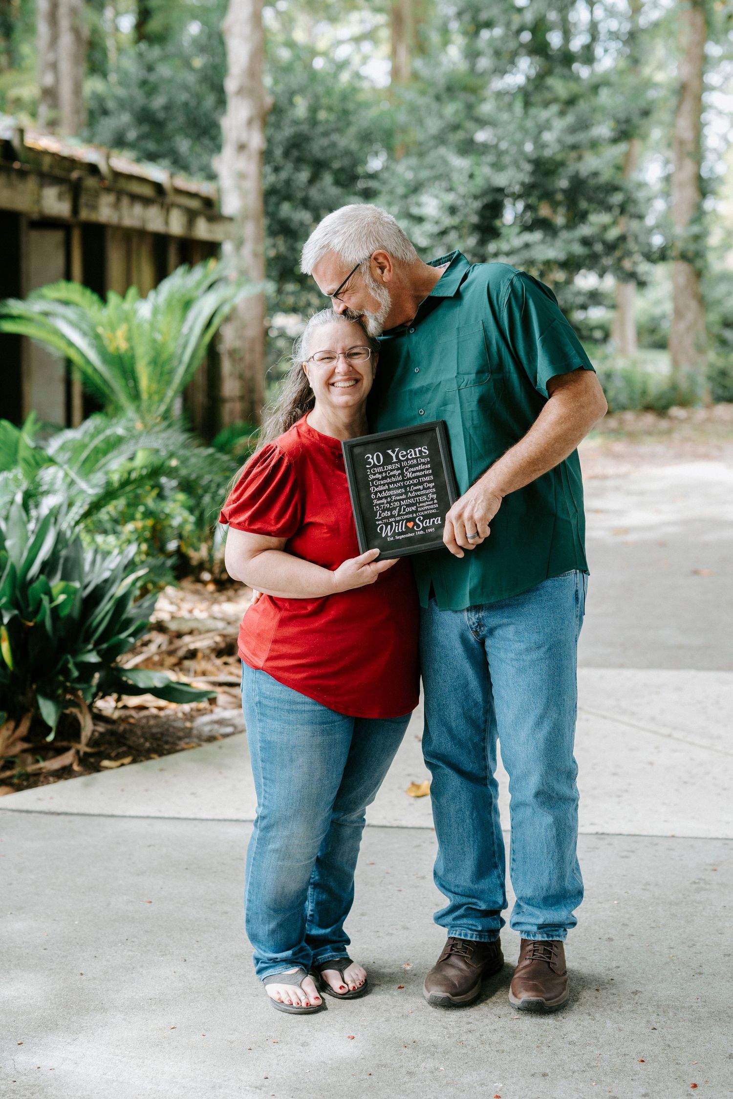 A couple shares tender moments in the garden while wearing casual clothing and standing together on a concrete path.