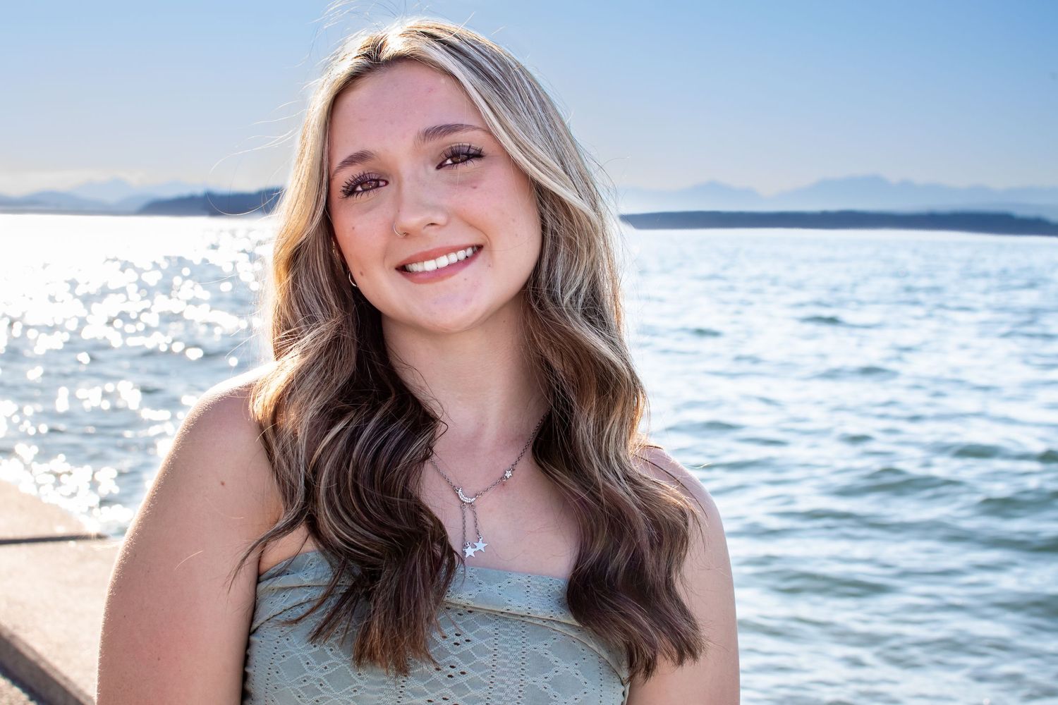 Close-up portrait of a smiling senior girl with soft golden hour light at Seattle’s Alki Beach.