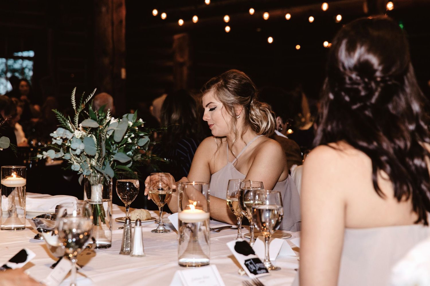 Elegant wedding reception tables with decorative candlelight and twinkling lights overhead create a romantic atmosphere.