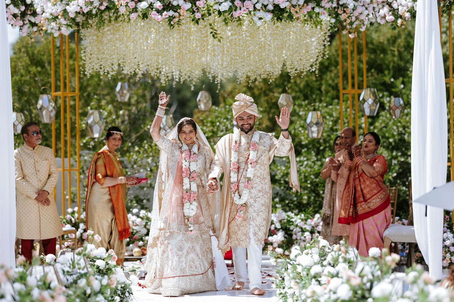 A traditional Indian wedding ceremony takes place under a white floral mandap decorated with elegant white flowers and draping.