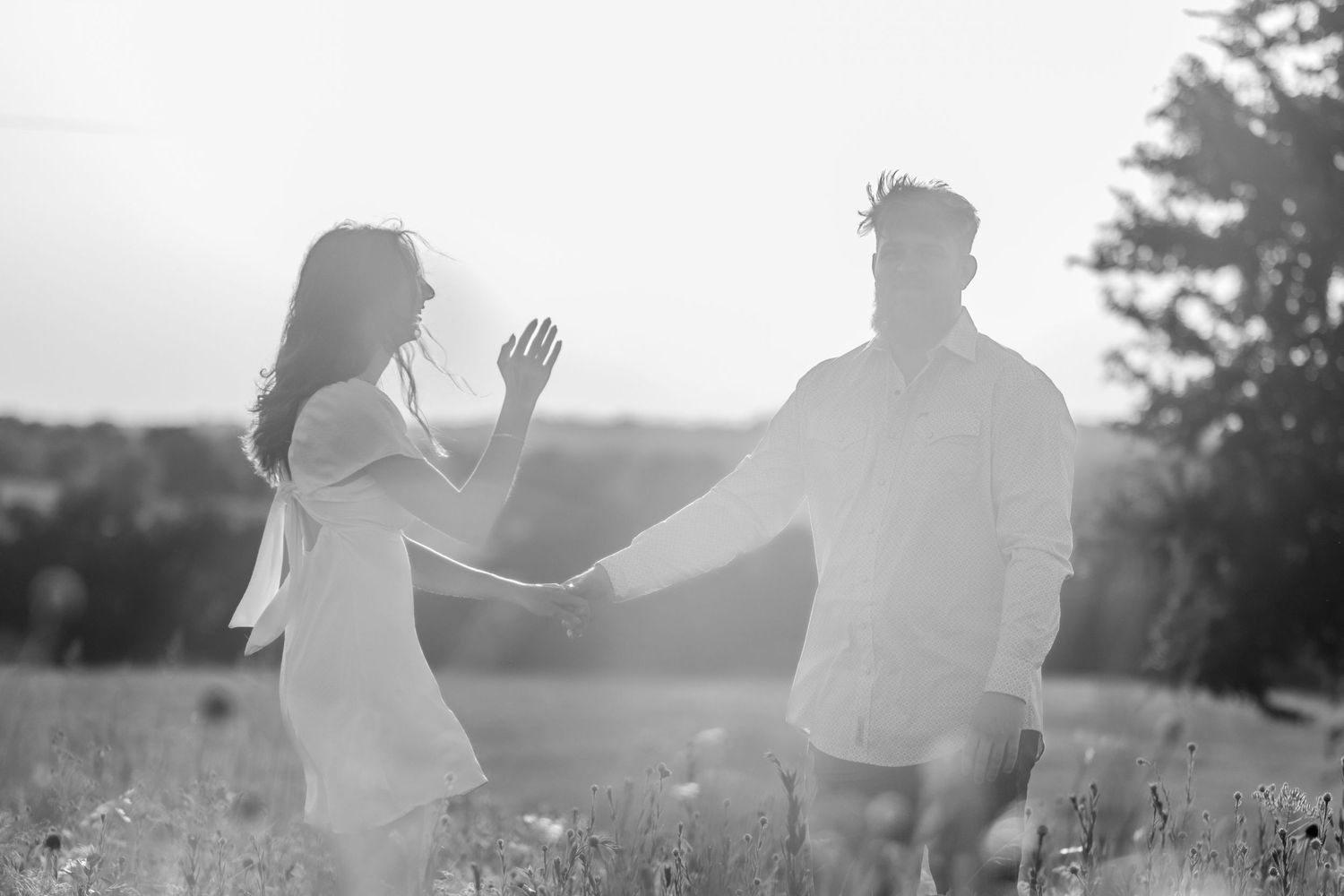 Silhouetted figures dancing and embracing in sunset field.