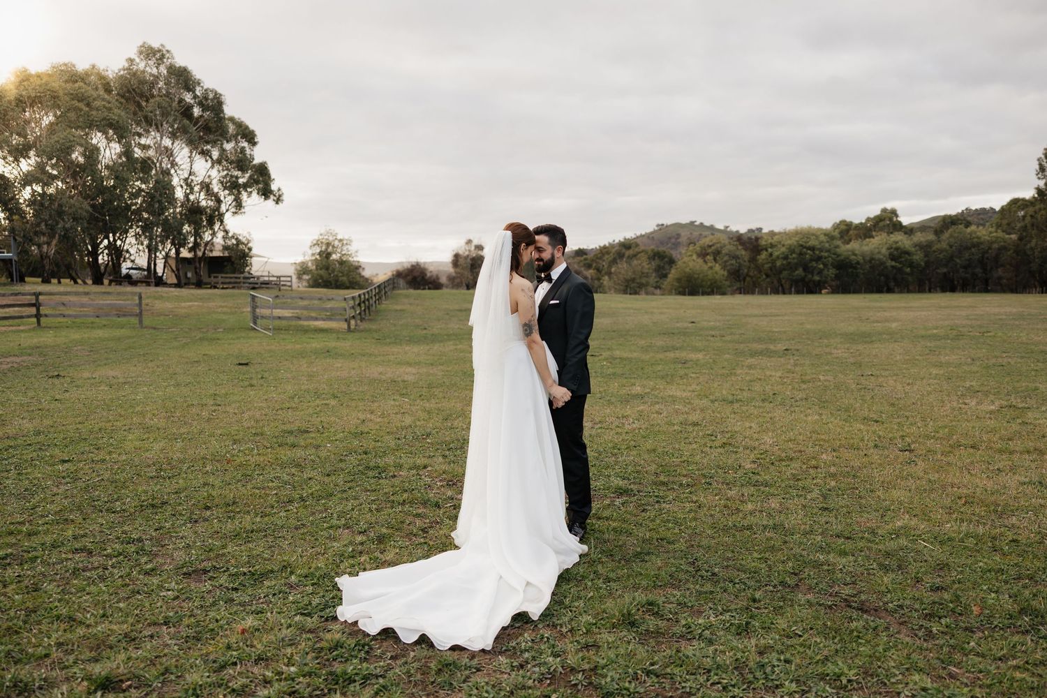 A couple in wedding attire walks through a scenic grassy field during their outdoor countryside wedding celebration.