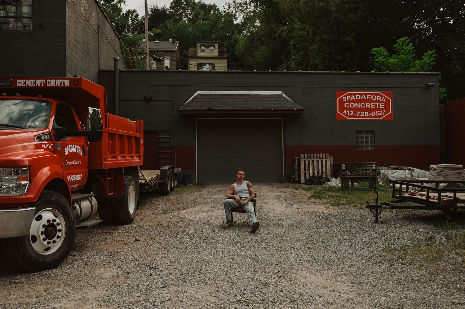 Red dump trucks and equipment parked in a gravel lot outside a rustic building in a wooded area.