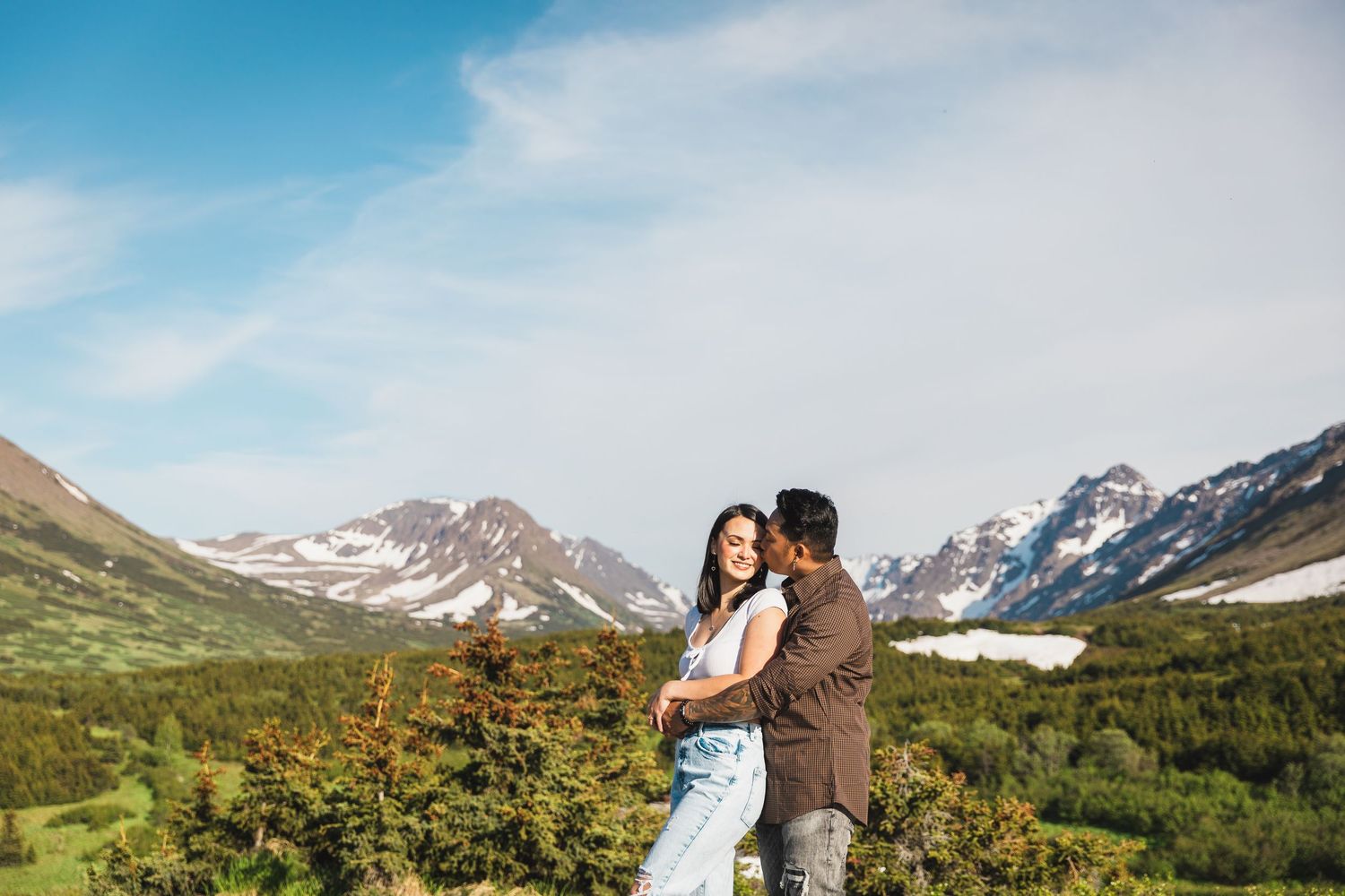 Family enjoying tender moments together outdoors in a grassy field with mountains in the background.