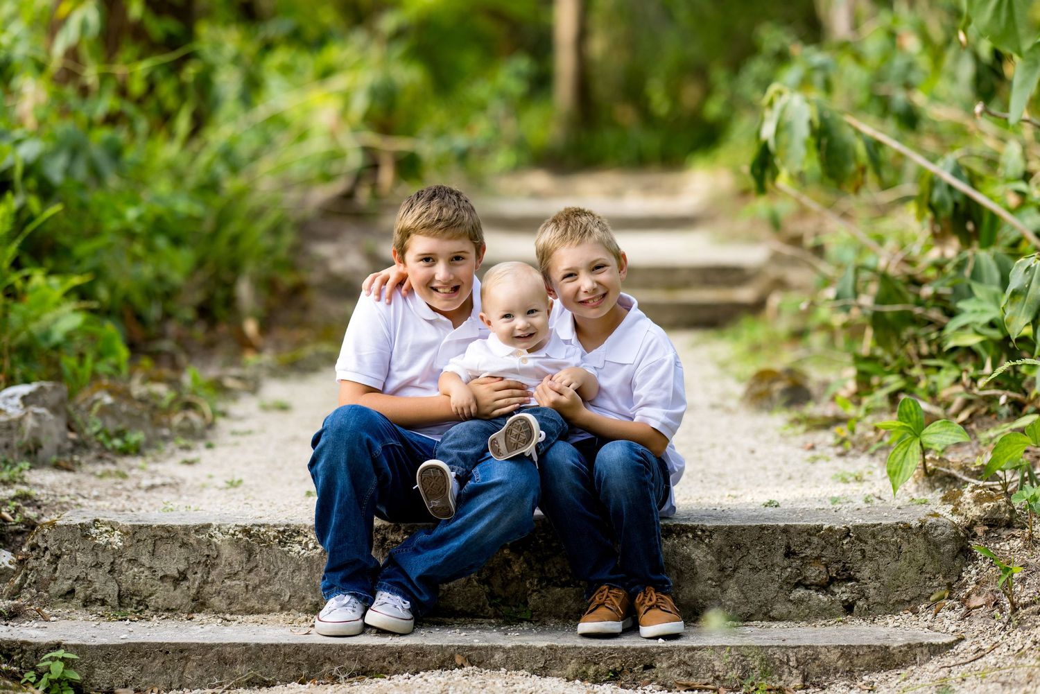 A family sits together on stone steps surrounded by lush greenery in a natural outdoor setting.