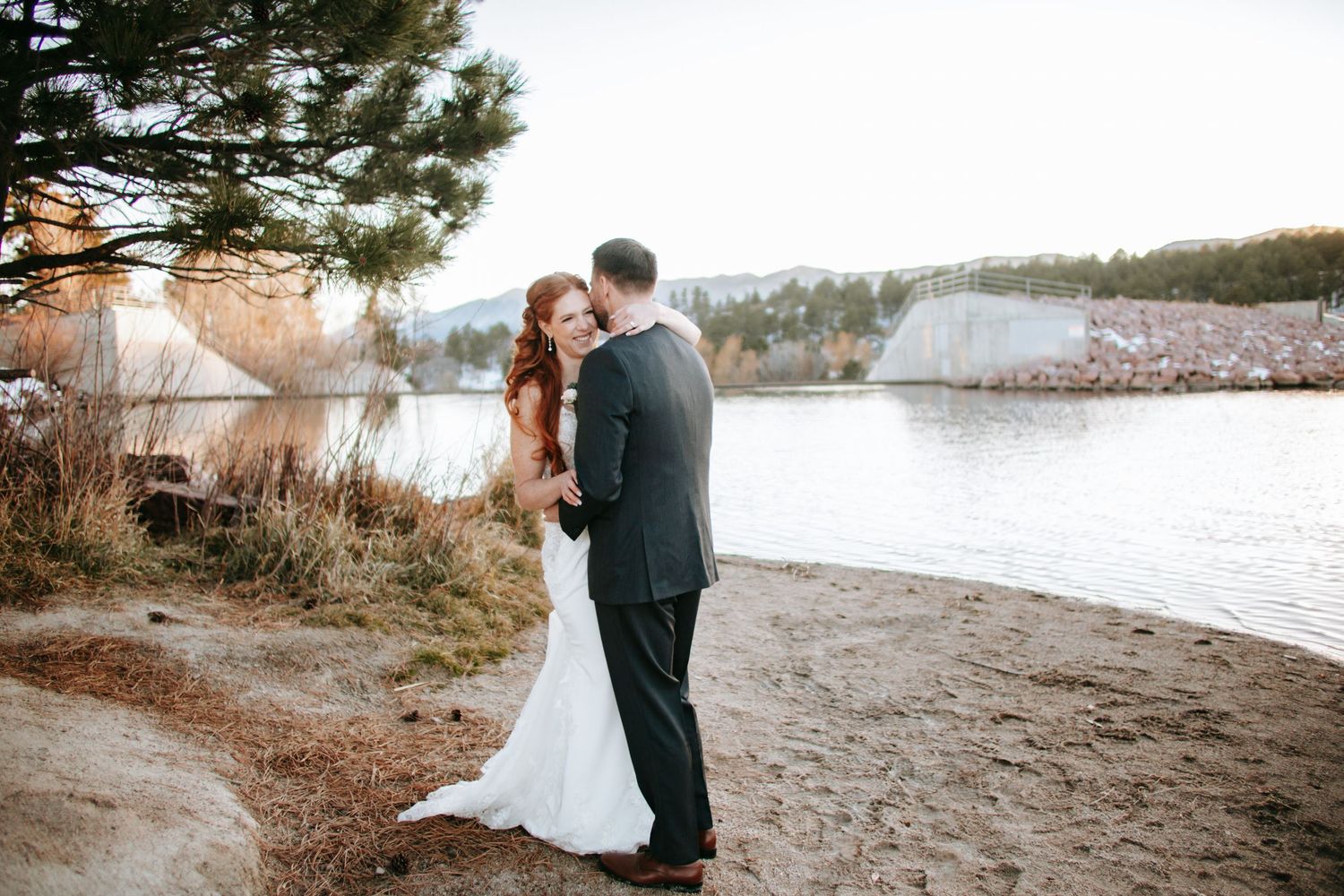 A couple shares an intimate moment on the shore of a lake during a winter wedding photoshoot.