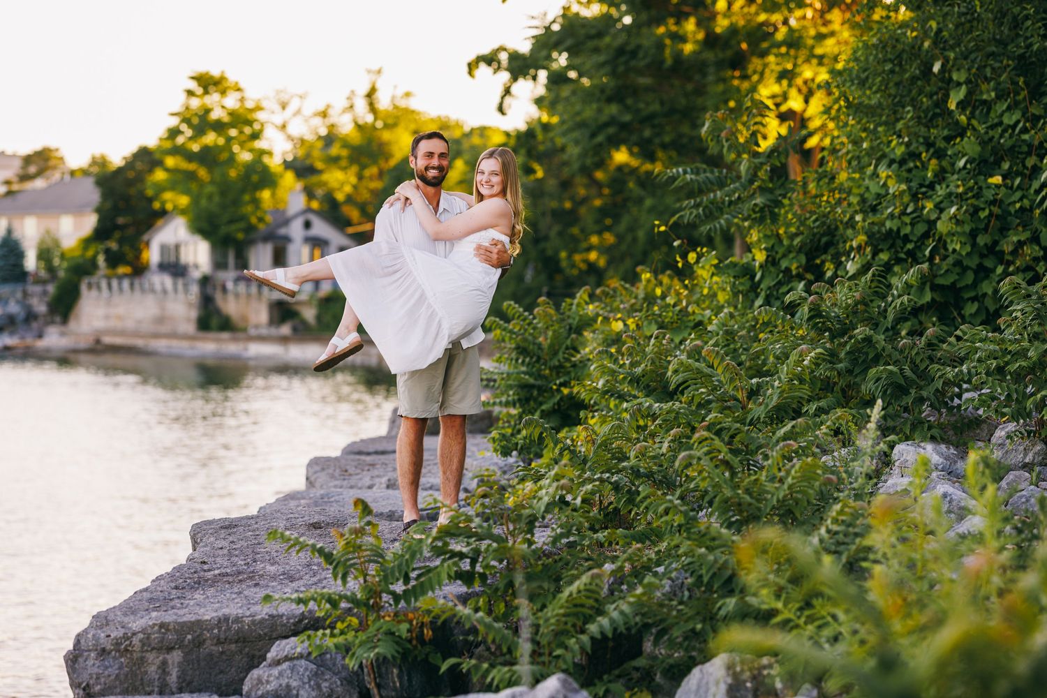 A couple enjoying a romantic evening photoshoot on large rocks by a scenic waterfront during golden hour.