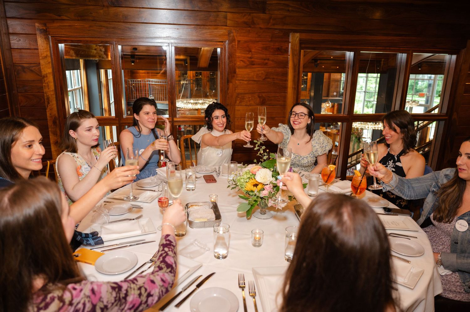 Women raising glasses in a toast at an elegant wooden dining room during a celebratory dinner party.