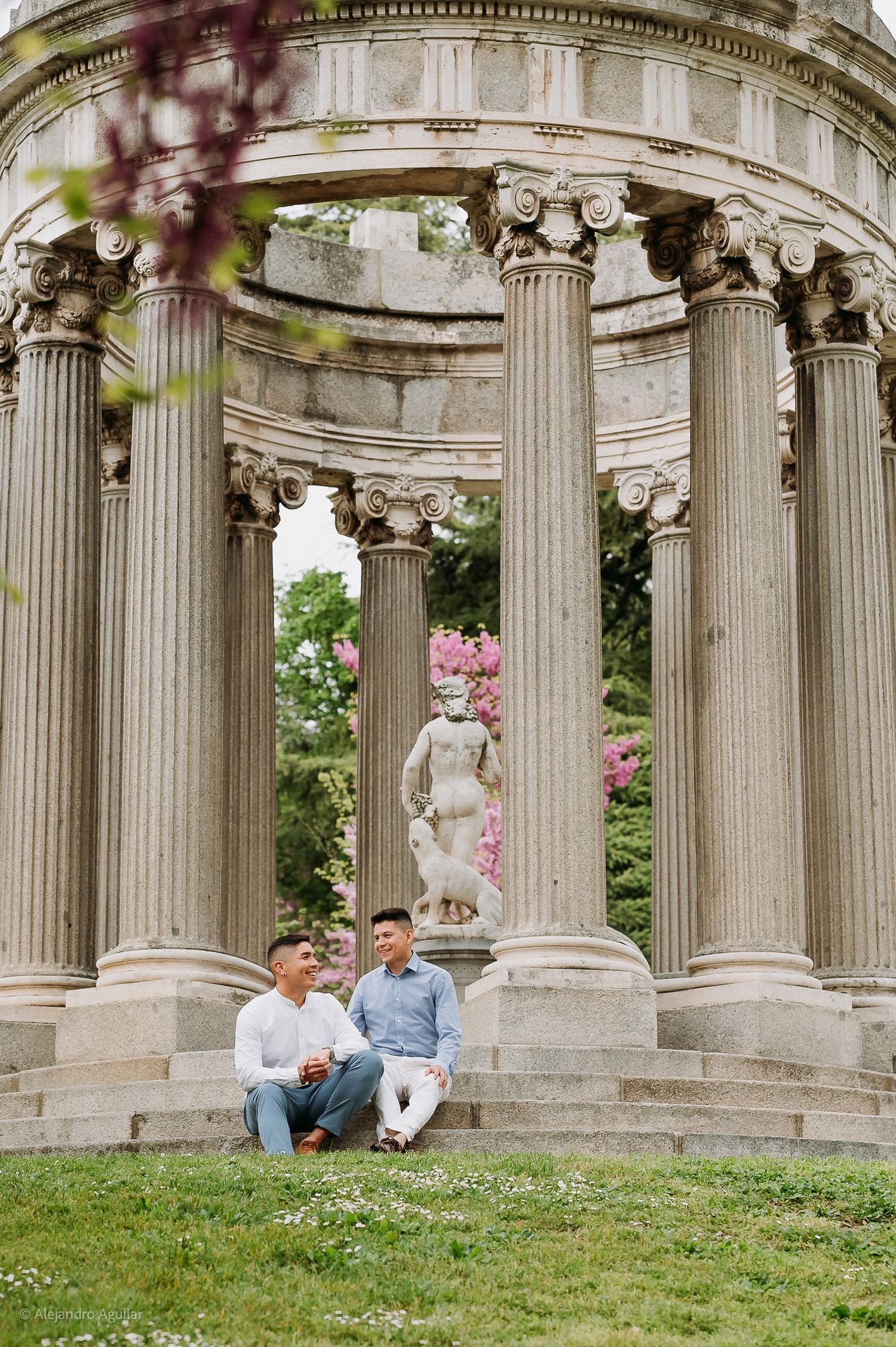 Two men sitting and talking on steps of classical rotunda with Ionic columns and statue.