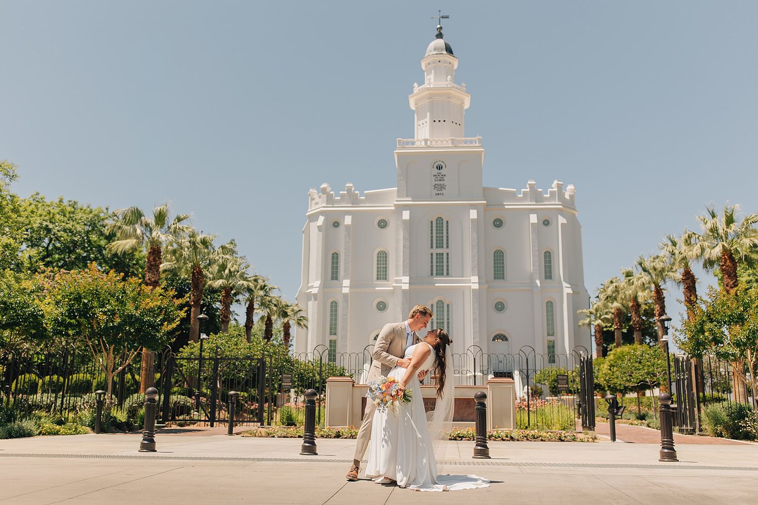 Bride and groom kissing in front of St. George Utah LDS Temple on sunny wedding day.