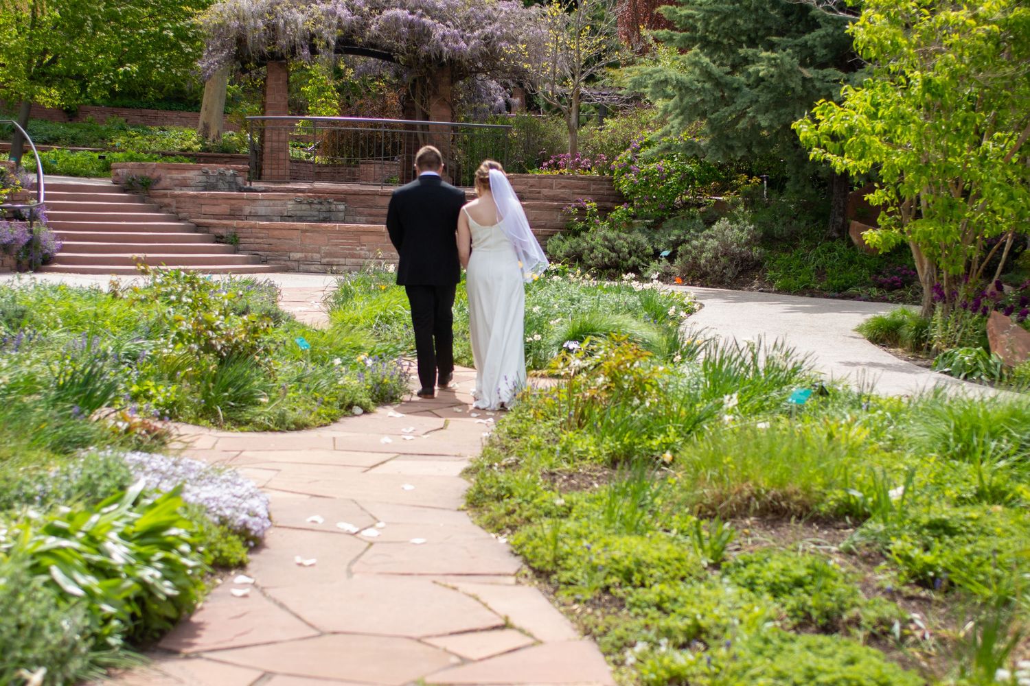 Couple walking along a winding stone path through a lush garden setting during a wedding photo session.