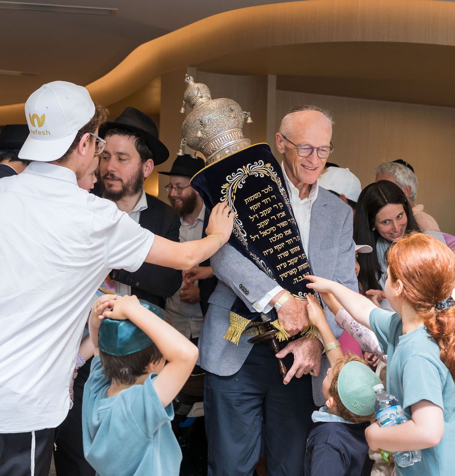 A group gathers around a decorative Torah scroll being held during a religious ceremony.
