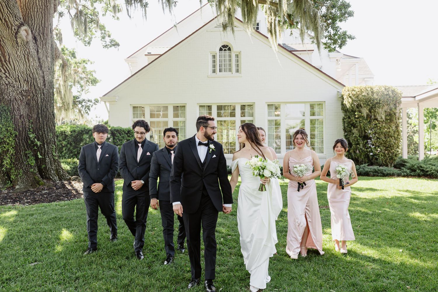 Black and white photo of a bride and groom walking through a lush garden, bride holding bouquet in wedding dress.