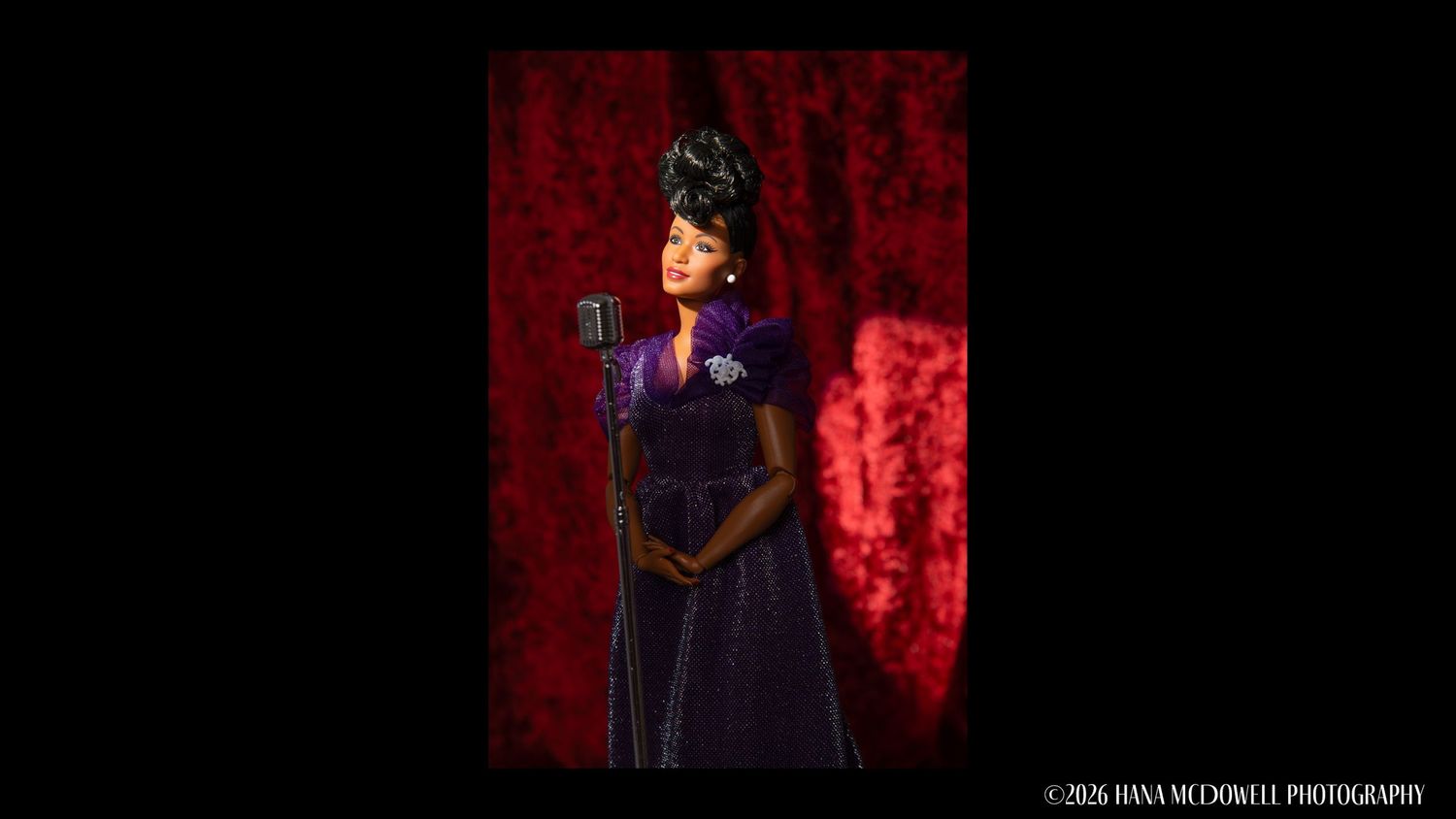 Woman in purple gown singing at a vintage microphone on a dark stage with red backdrop.