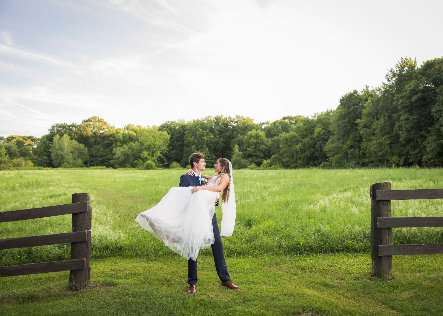 Newlyweds share an intimate moment outdoors with autumn foliage and rustic architecture in background.