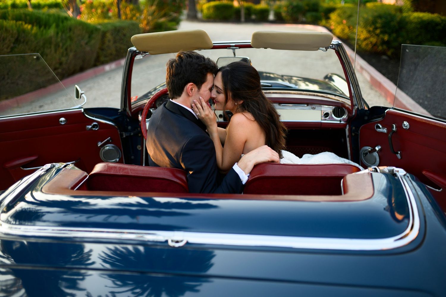 Newlyweds go in for a kiss while sitting in a blue vintage car with red leather seats in front of the Palm Event Center. in Pleasanton.