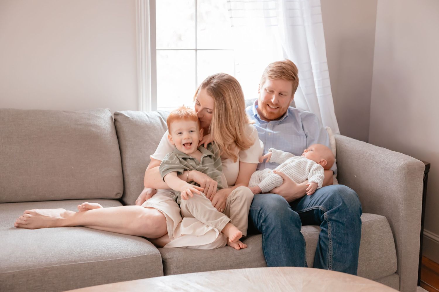Family relaxing together on a gray couch at home in a bright living room.