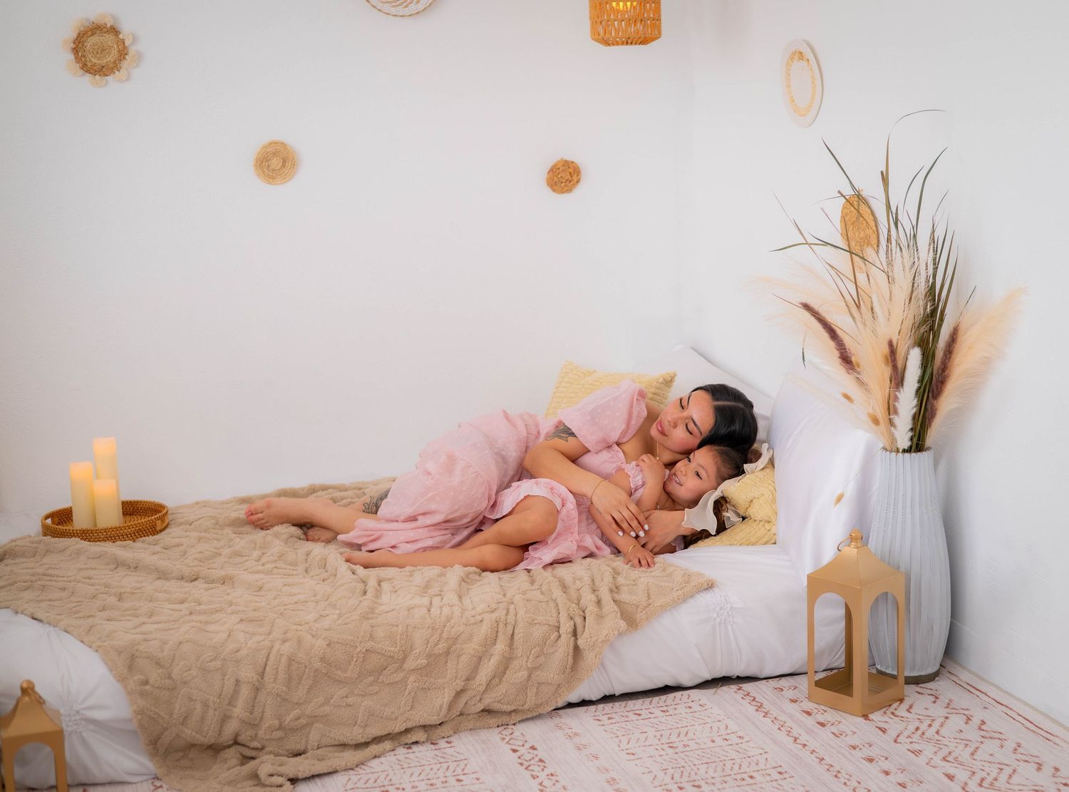 Cozy bedroom scene with warm lighting, pampas grass in white vase, and soft beige bedding against white walls.