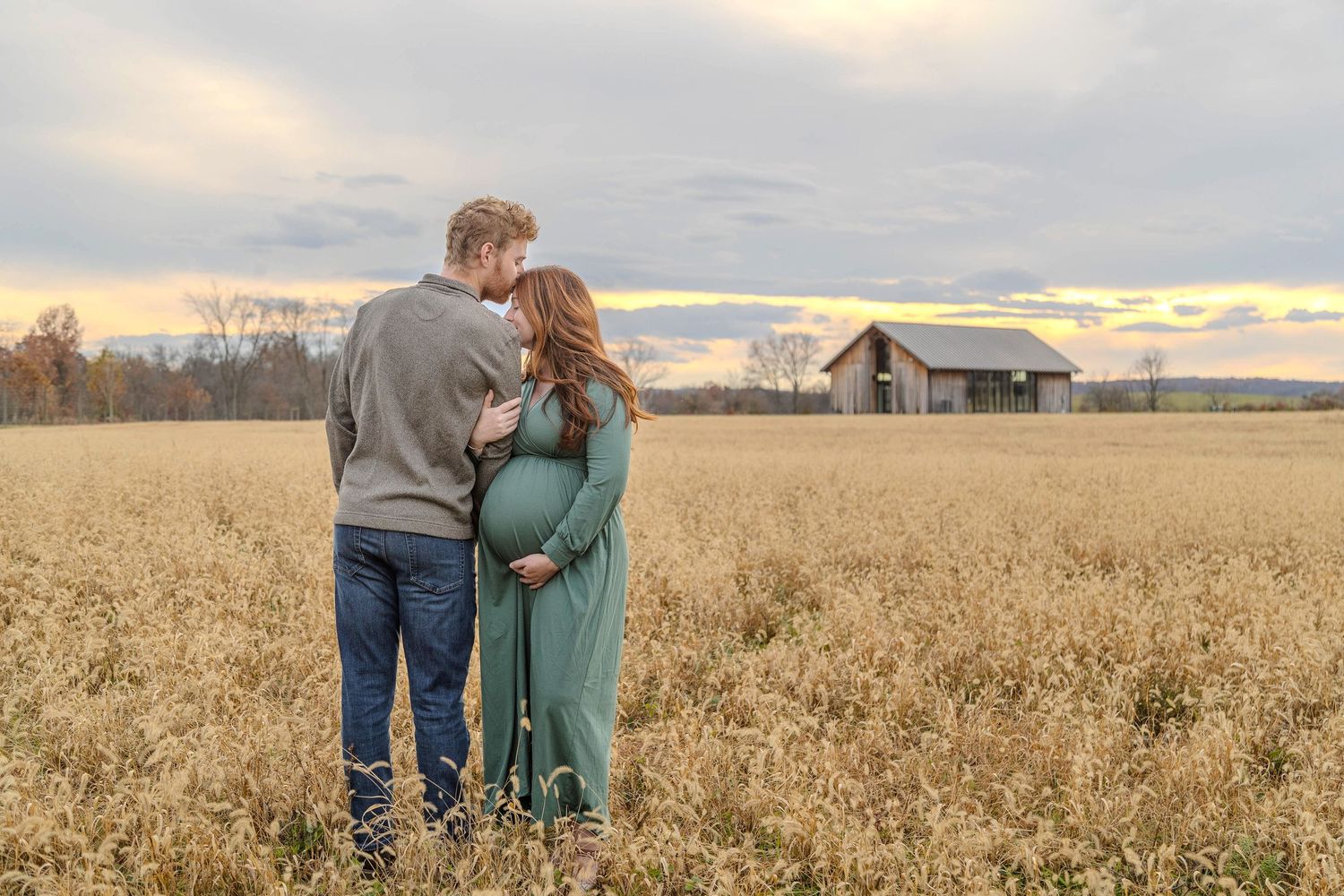 A couple and child lay together in a golden wheat field during sunset.