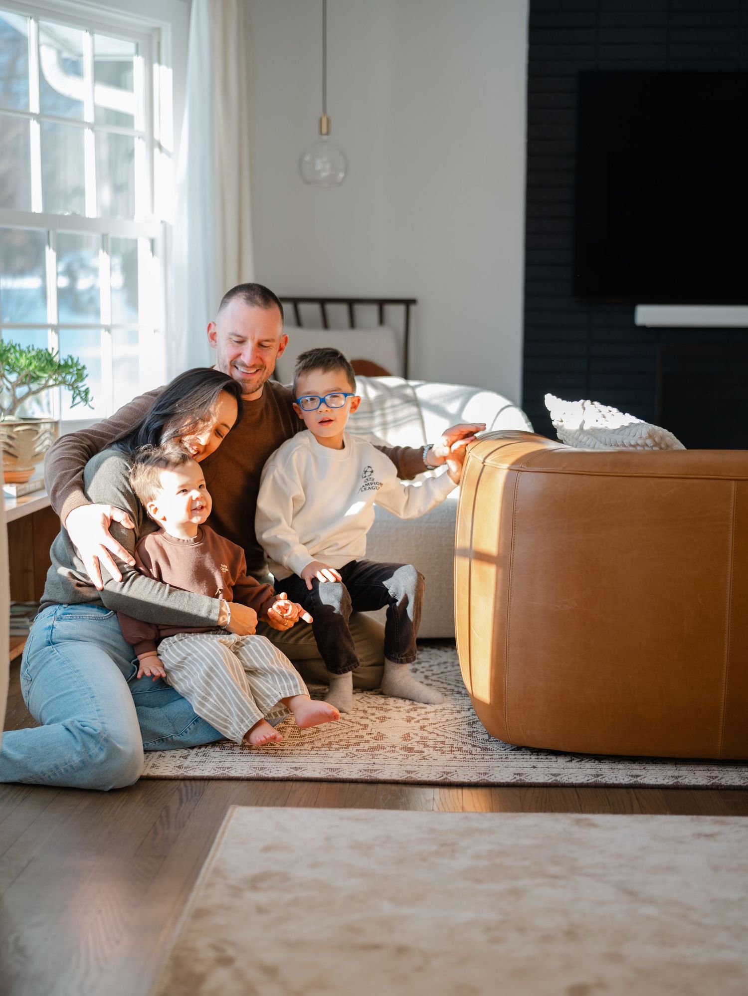 In-home family photo session in Monmouth County New Jersey with parents cuddling their children in front of a snowy window.