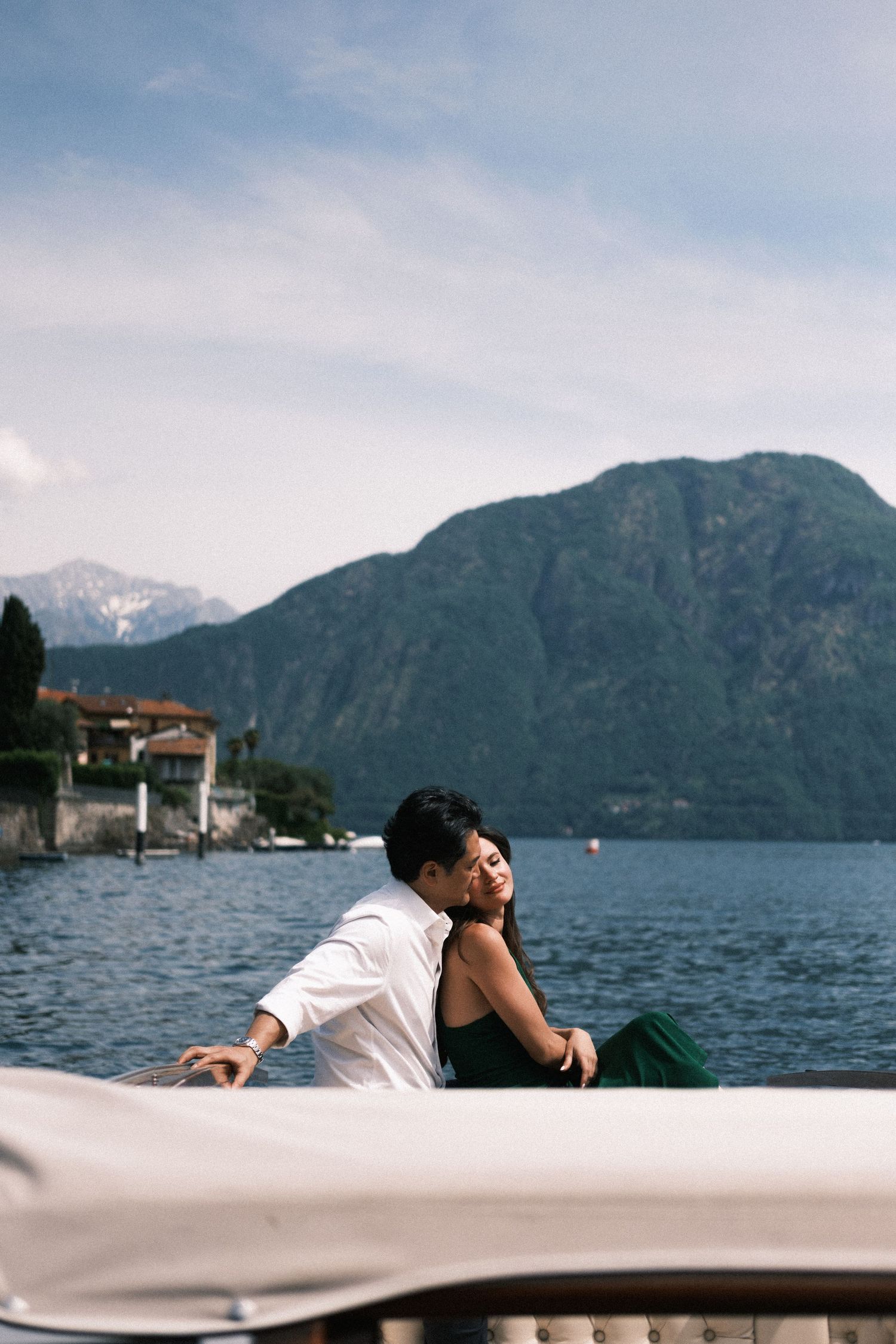 Elegant couple sitting together on a luxury boat with scenic Italian lakeside village in the background.