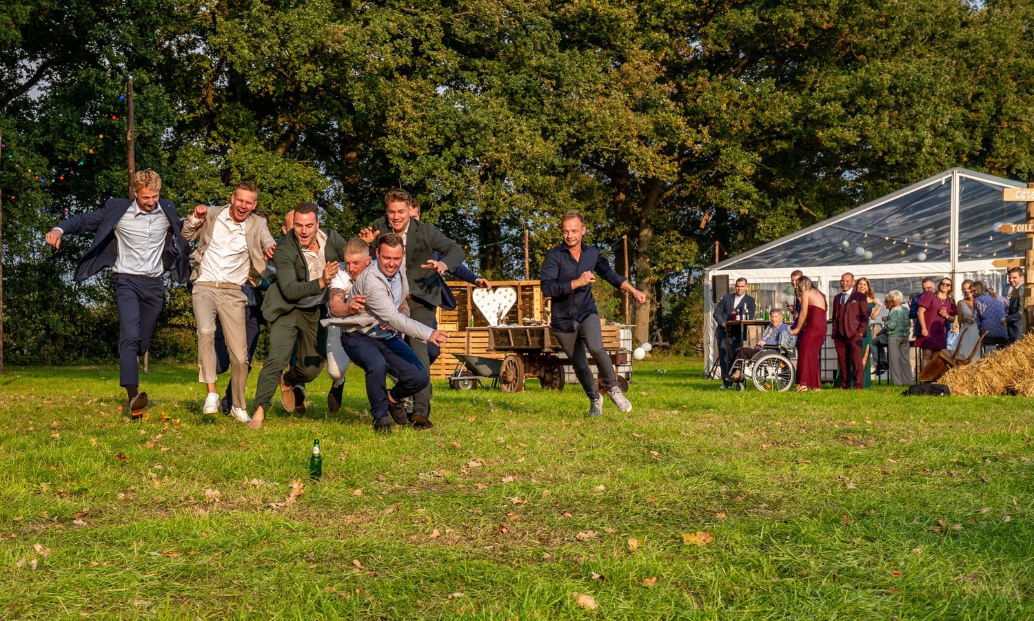 Een groep mannen neemt deel aan een touwtrekwedstrijd tijdens een bruiloftsreceptie in de buitenlucht.
