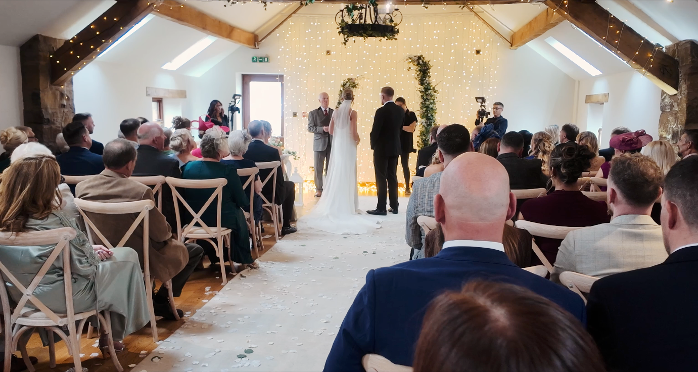 Elegant barn wedding ceremony with guests seated in rows as couple exchanges vows at floral altar.
