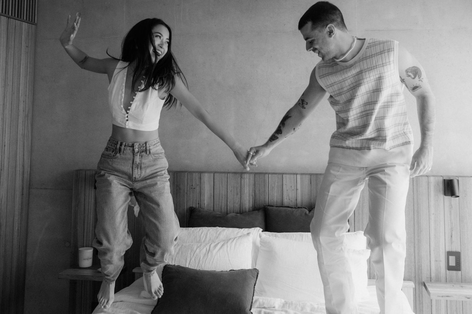 Black and white photo of a couple jumping and playing on a bed together.