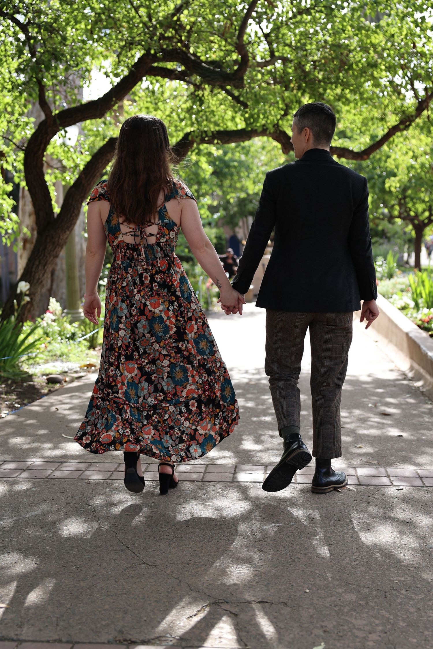 A couple walking hand in hand on a garden path wearing coordinated outfits.
