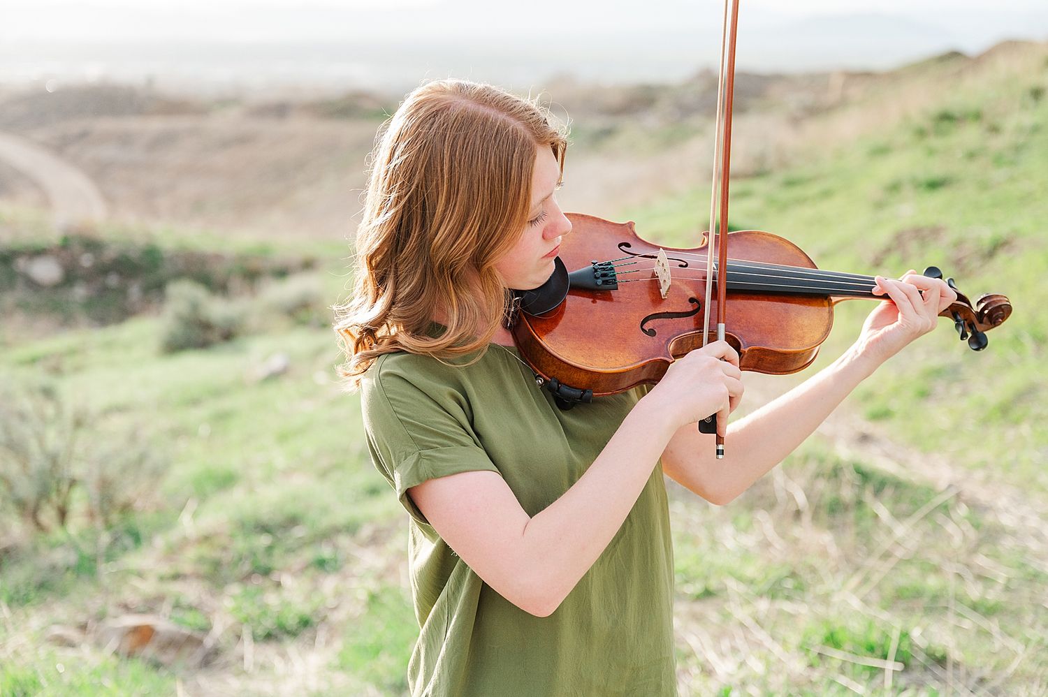 Violinist practicing outdoors in a natural mountain setting with warm lighting.