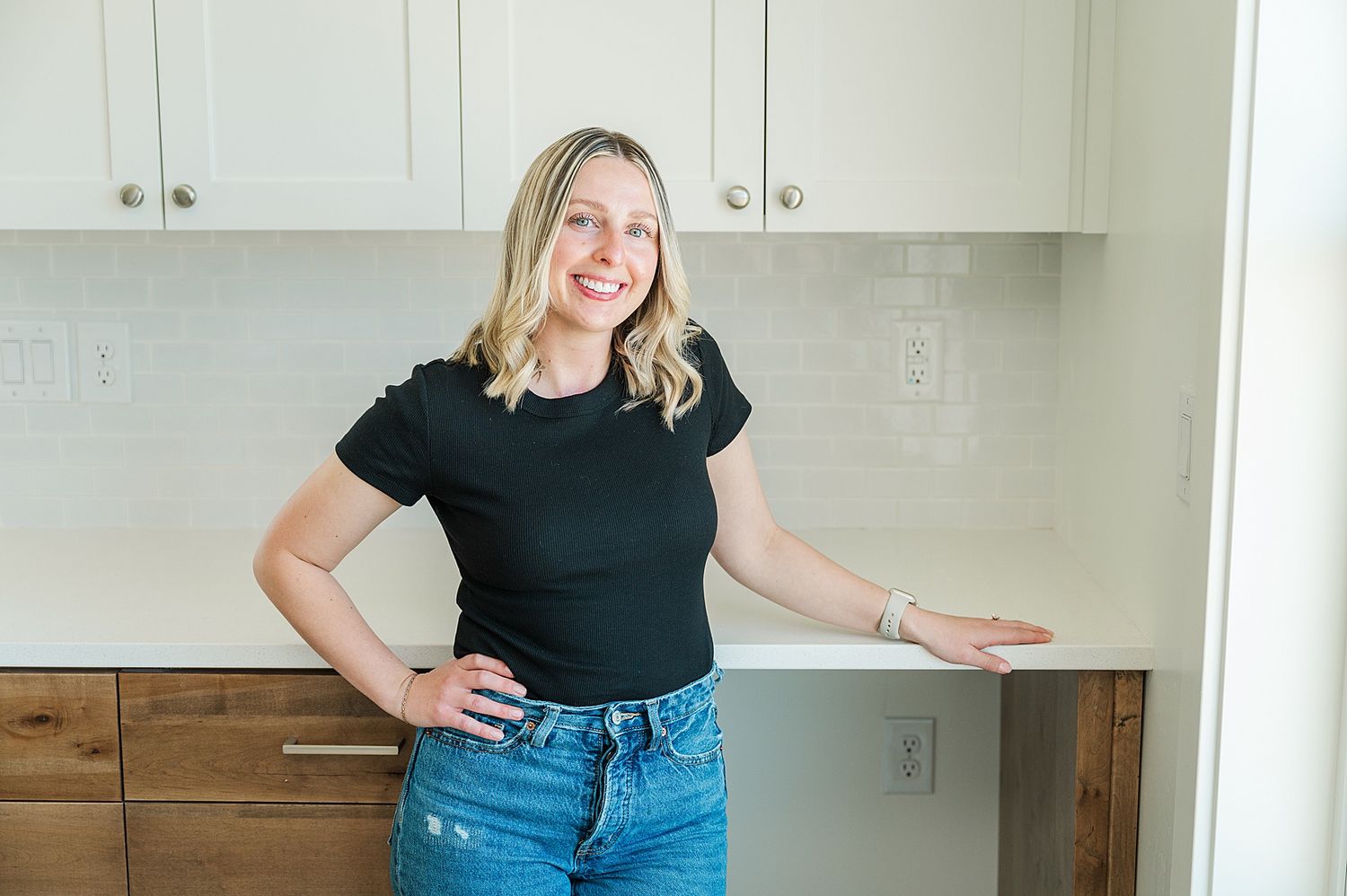 Person in casual attire strikes welcoming pose in modern kitchen setting.