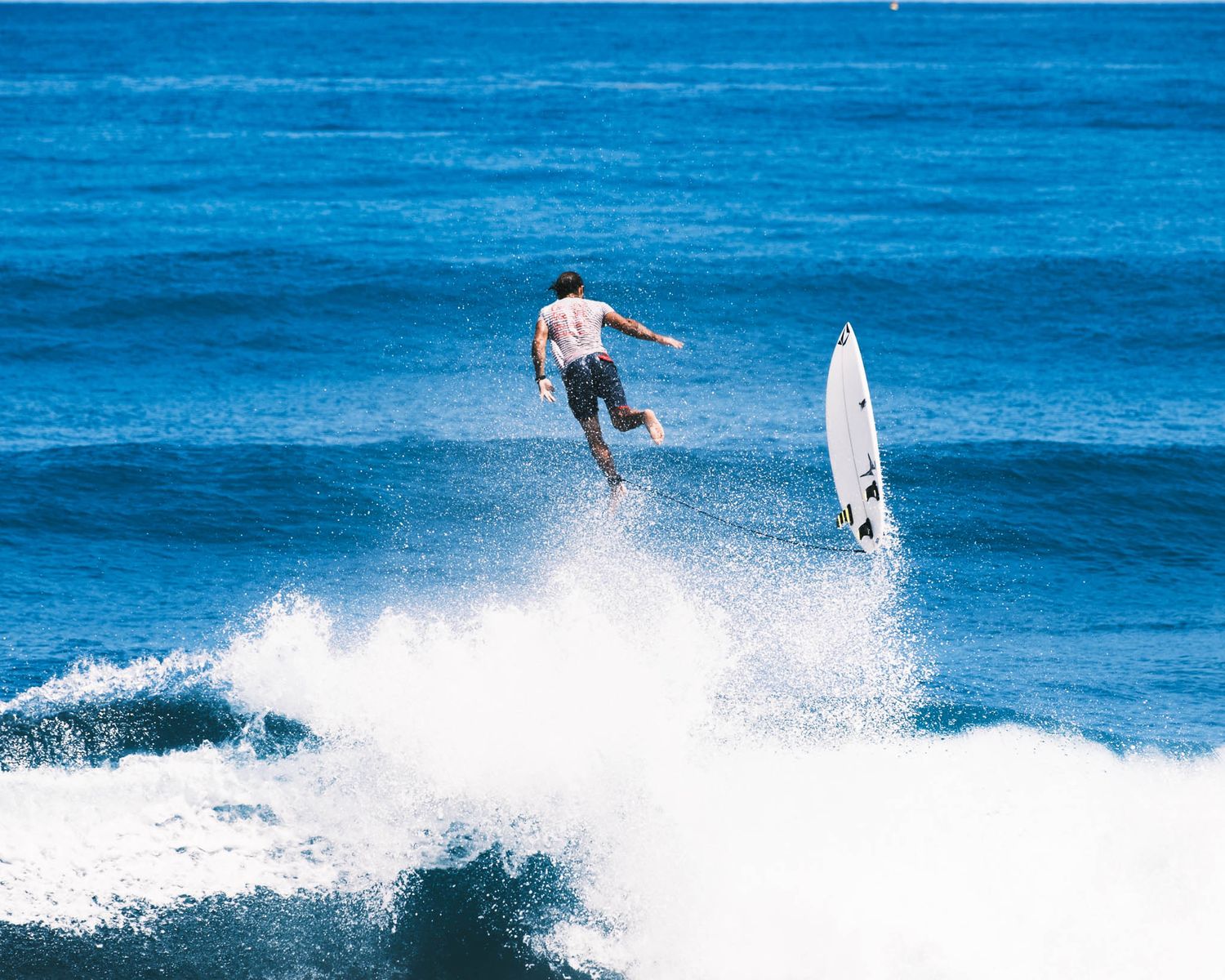 Surfer launches high above the wave while another surfer watches in the distance.