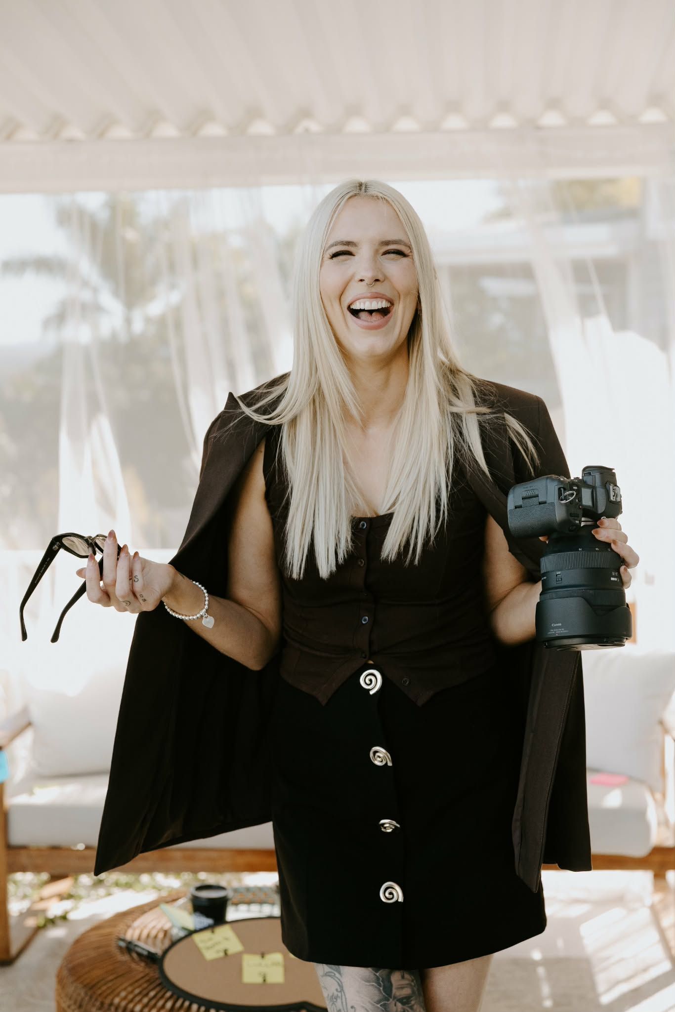 A series of photos showing someone in black clothing holding photography equipment and smiling with expressive gestures.