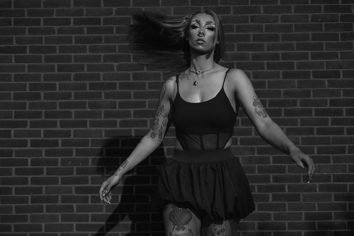 Black and white portrait of a dancer in a short dress posing gracefully against a brick wall.